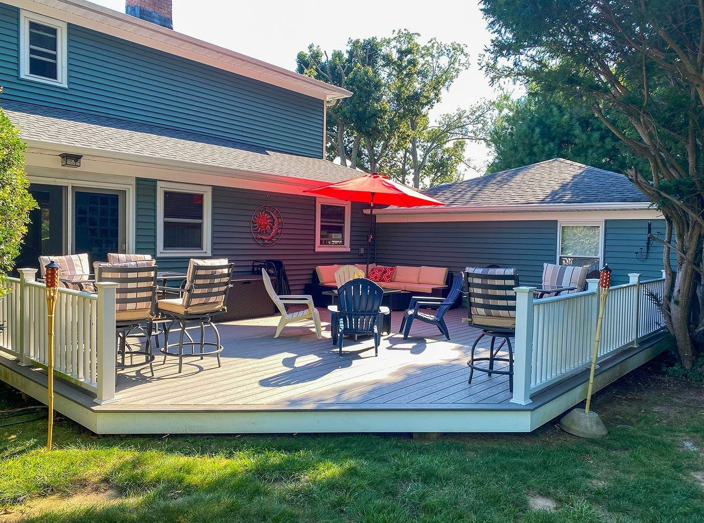 A backyard deck with seating, an umbrella, and attached to a blue house on a sunny day.