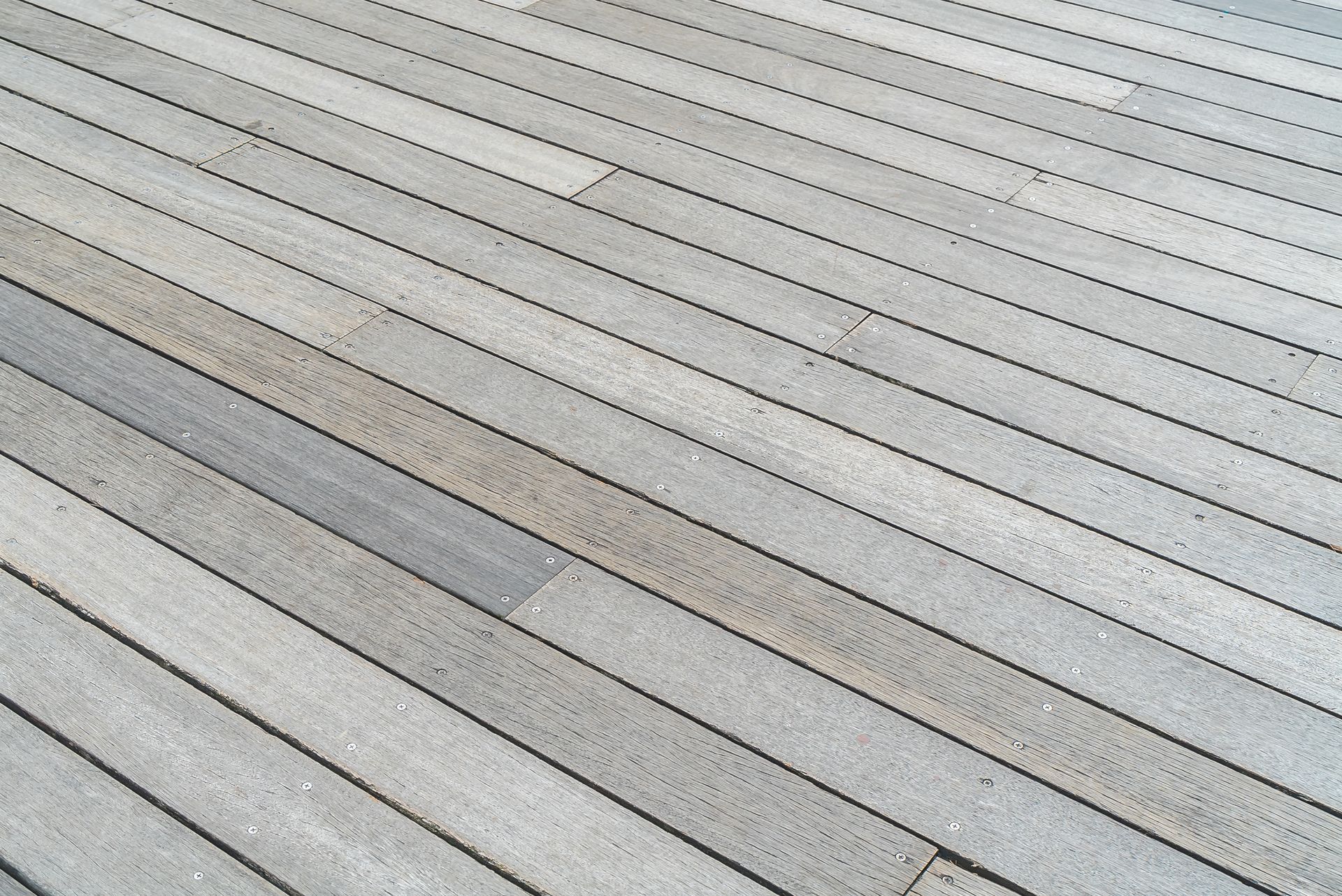 Diagonal view of light gray wooden decking with alternating planks and subtle weathered patches