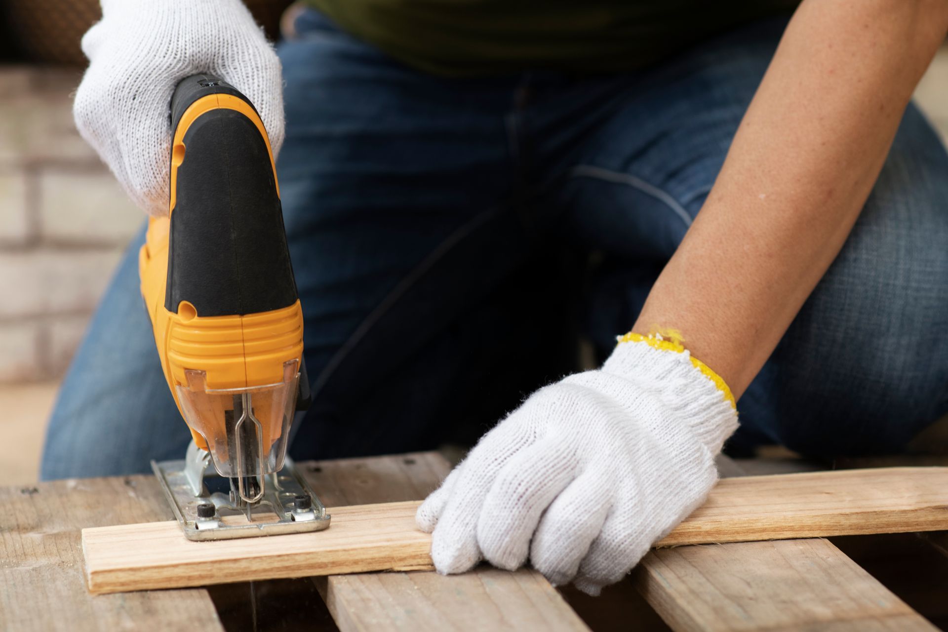 Gloved hands using a jigsaw to cut a wooden plank on a workbench