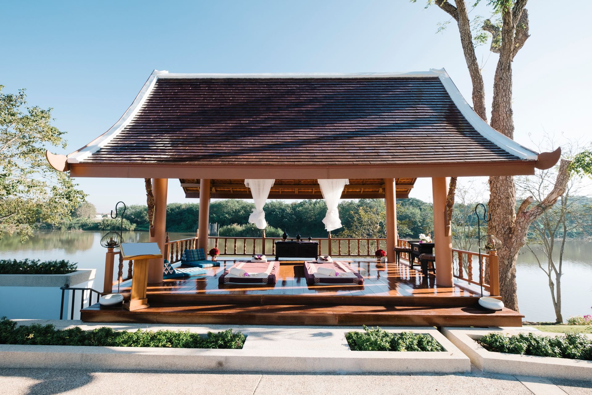 Open-air pavilion with a red roof, overlooking a calm lakeside in bright daylight