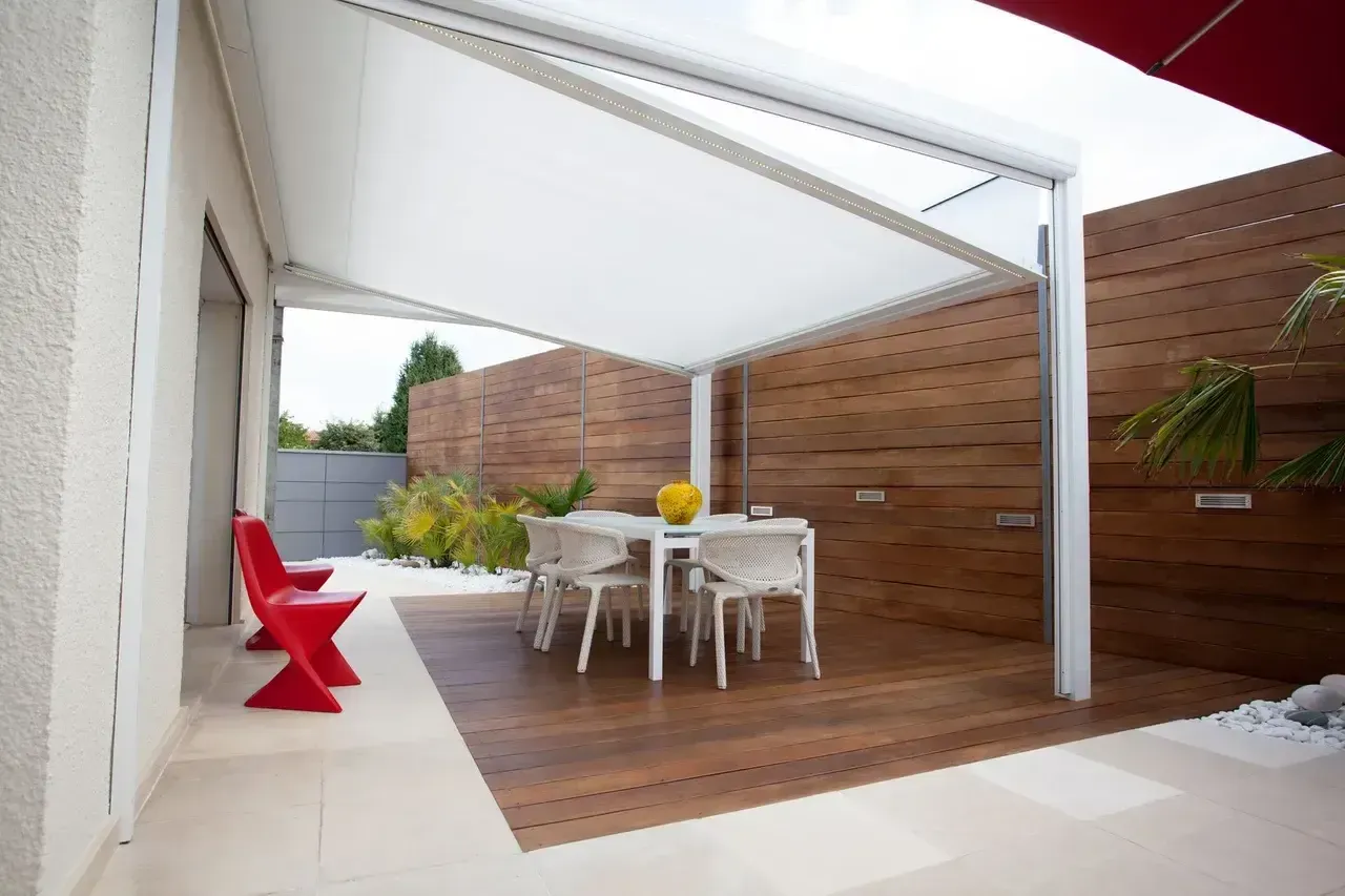 Outdoor dining area with a white canopy, wooden deck, table, chairs, and red chairs.