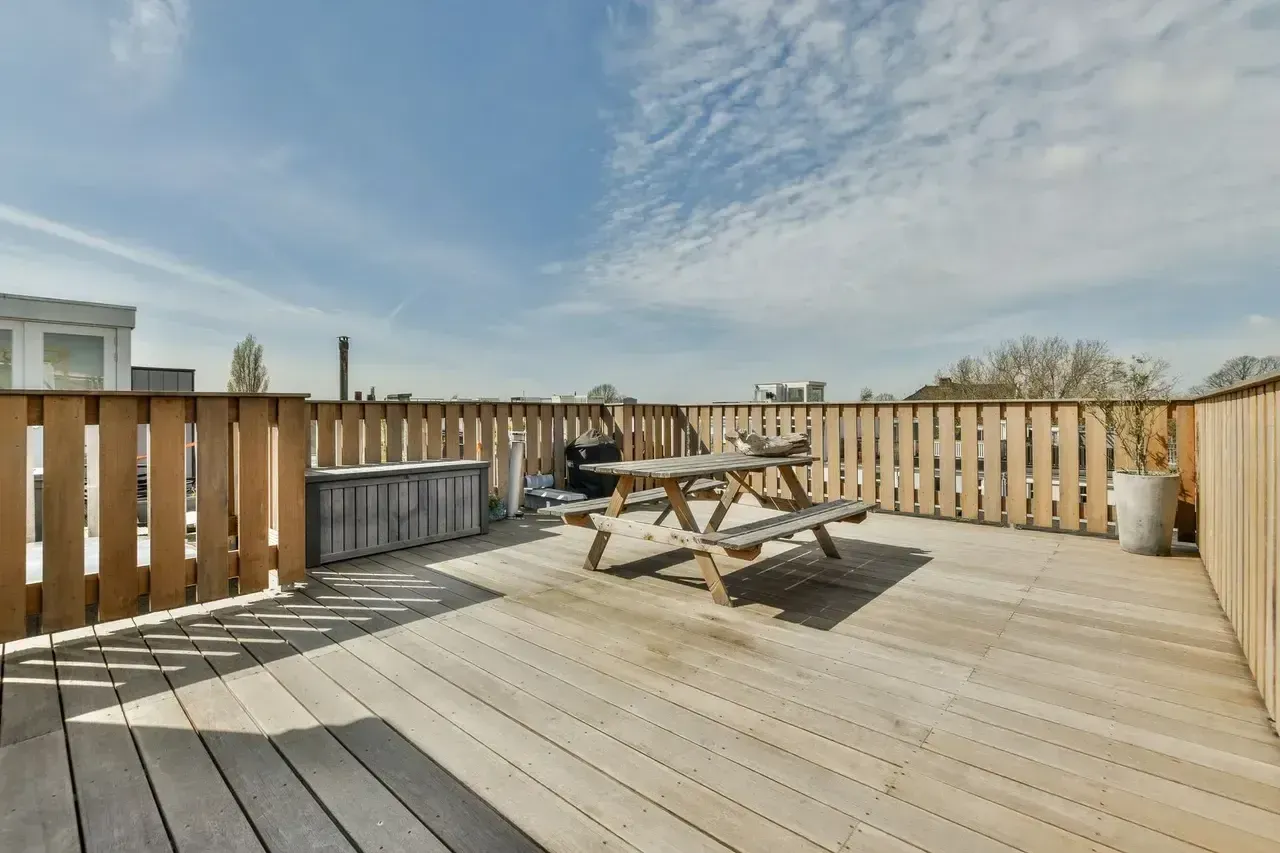 Wooden rooftop deck with a picnic table, fences, and blue sky.