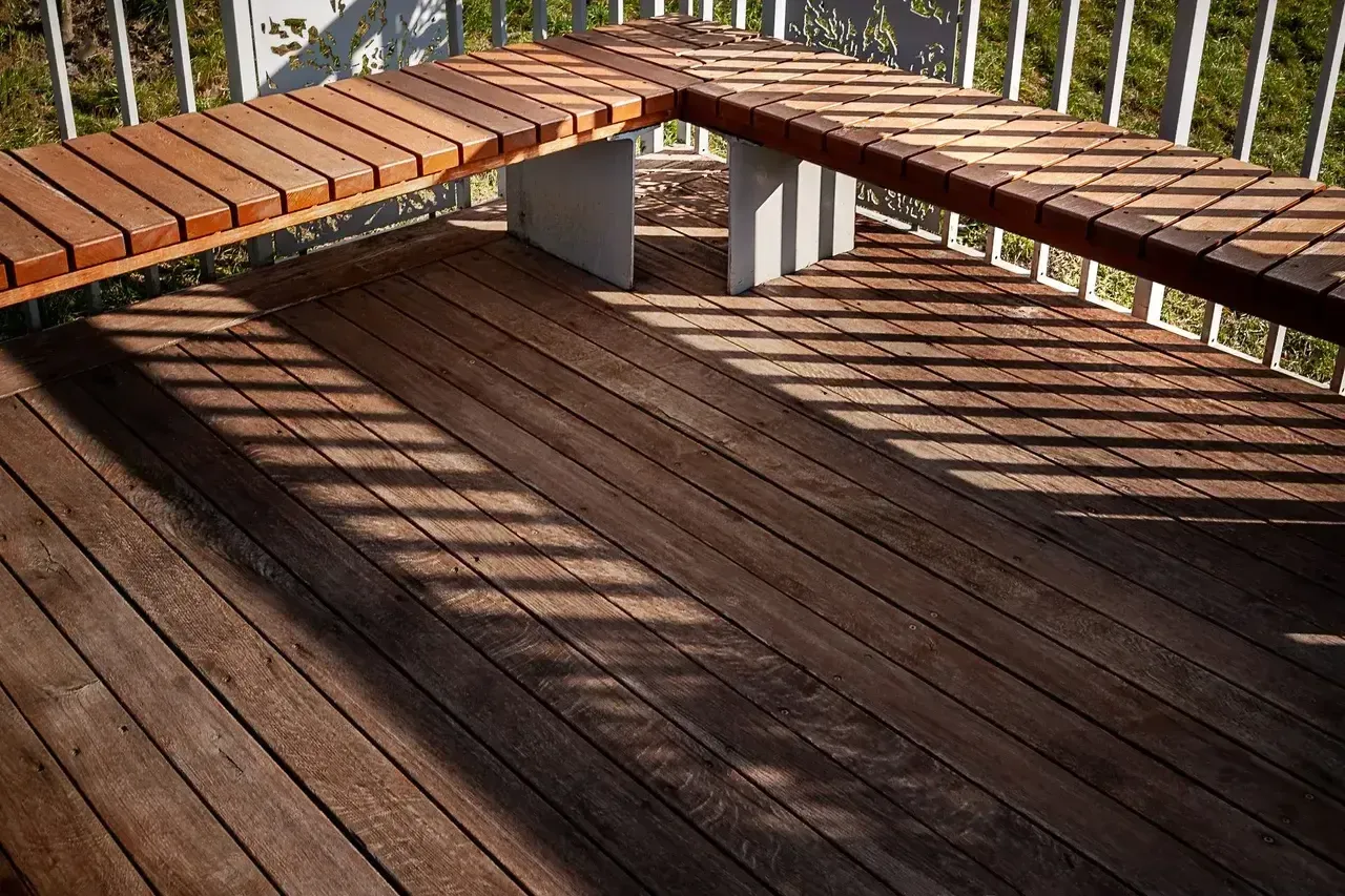 Wooden deck with built-in benches, angled against a white railing; sunny.