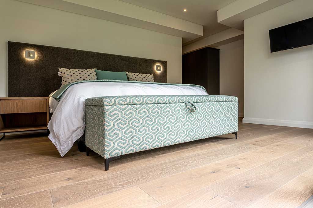 A bedroom with a bed , ottoman , nightstand and television.