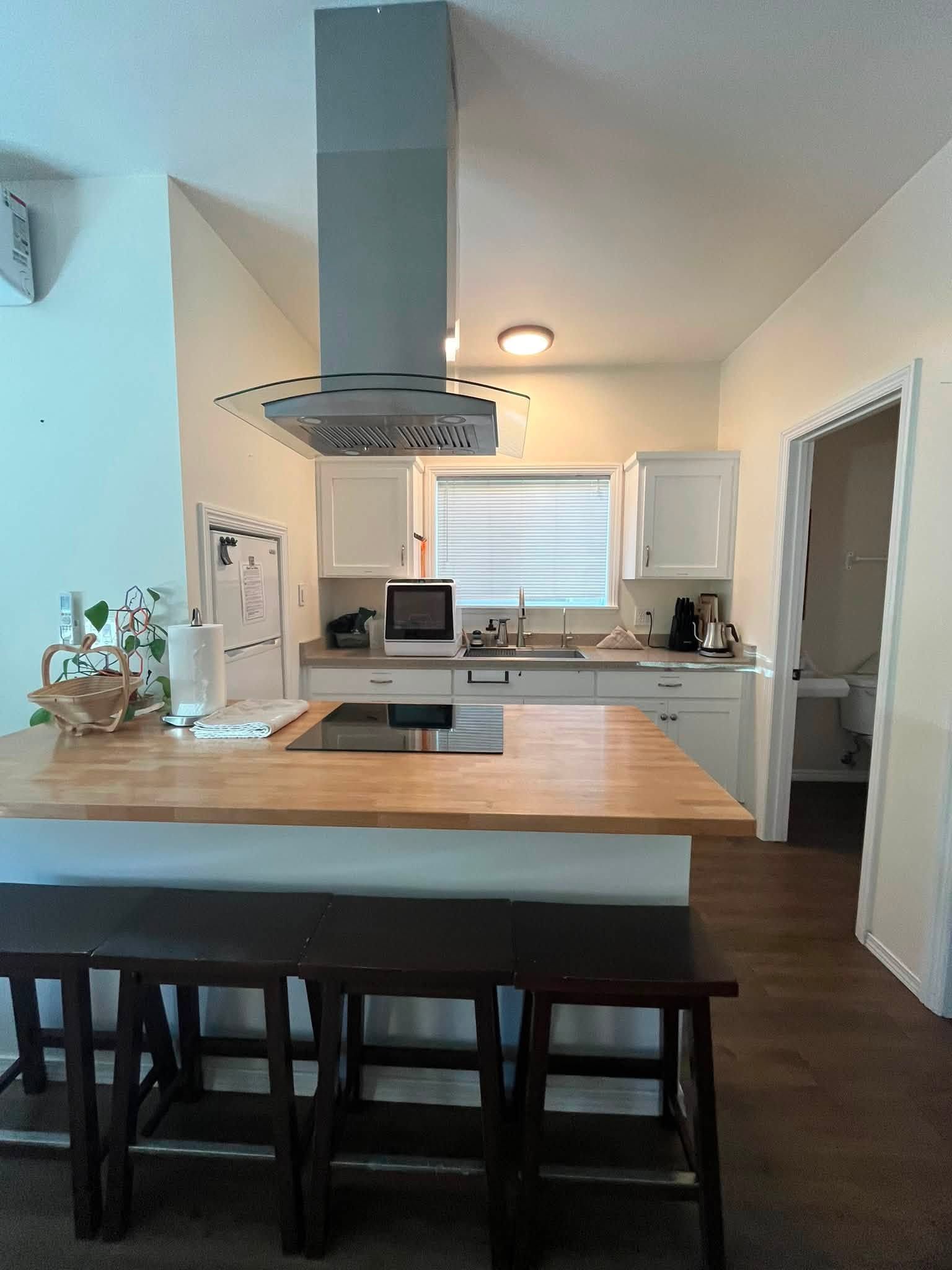 Modern kitchen with a large wood island, black stools, stainless range hood, and white cabinets.