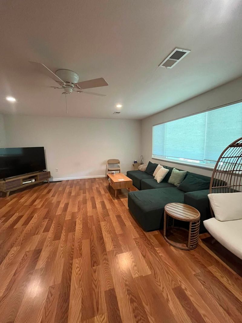 Modern living room with teal sectional, TV, wood floors, ceiling fan, and large window blinds