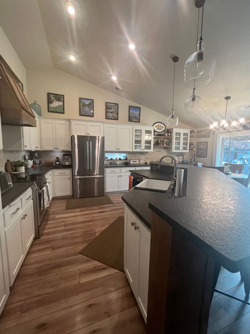 Spacious modern kitchen with stainless steel appliances, white cabinets, wood floors, and a dark island countertop.