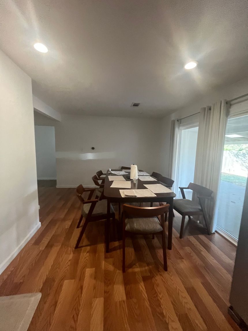 Dining room with wooden table and chairs, hardwood floors, and sliding glass doors to the right.