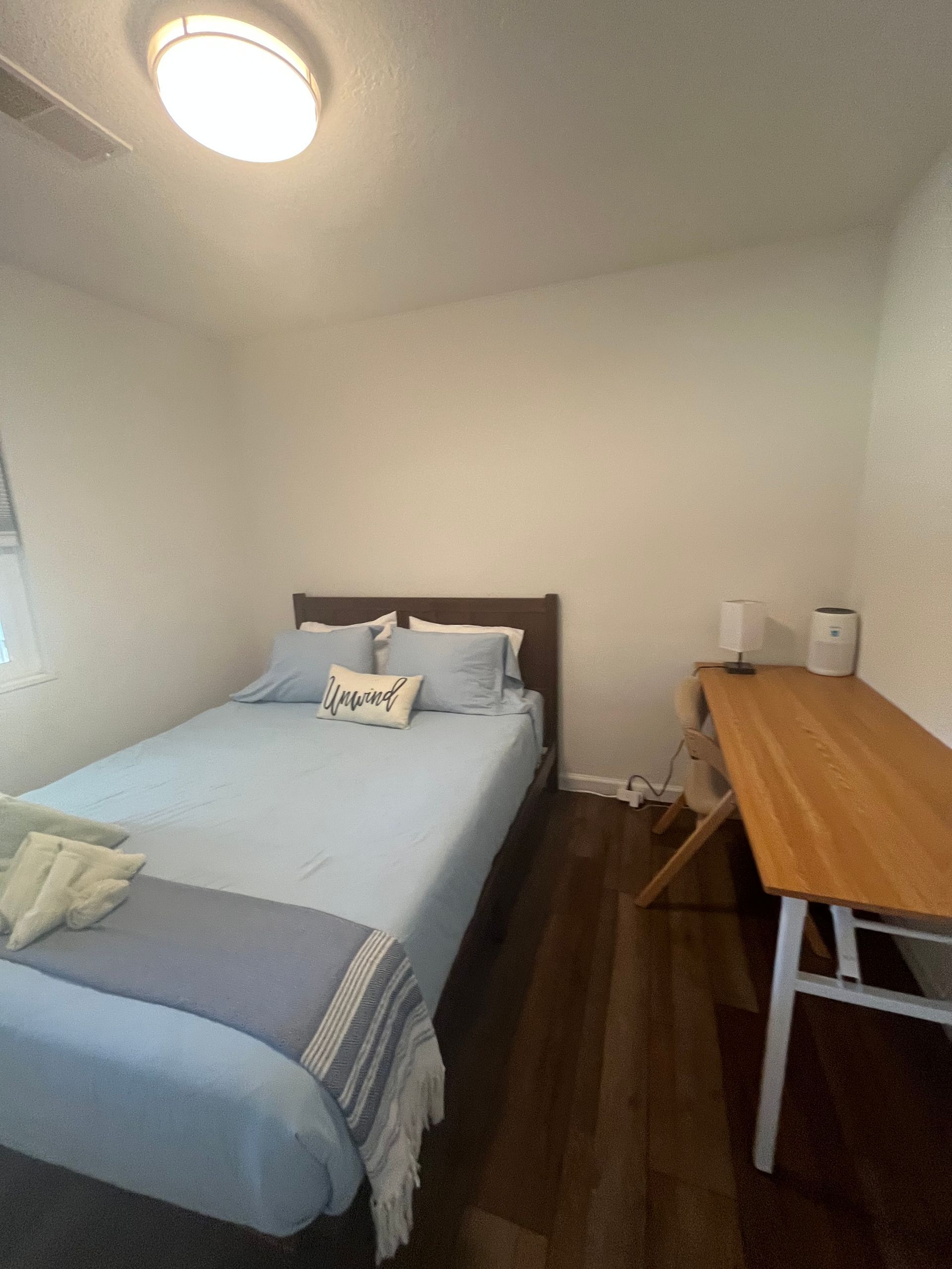 Small bedroom with a single bed, wooden desk, and white walls.