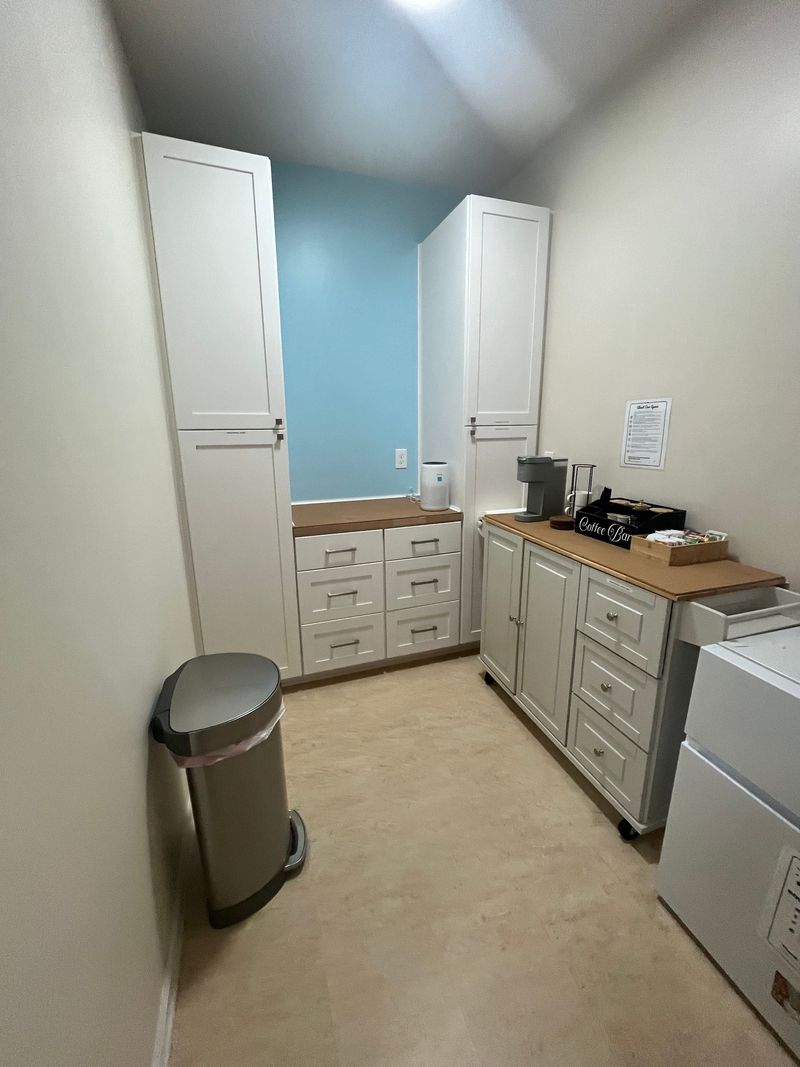 Small kitchen with white cabinets, blue wall, beige floor, trash can, and refrigerator.
