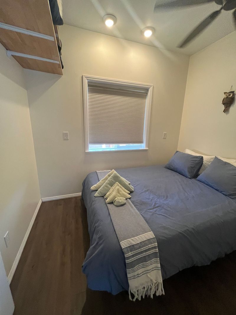 Small bedroom with a gray bed, window, wood floor, and sloped ceiling lights