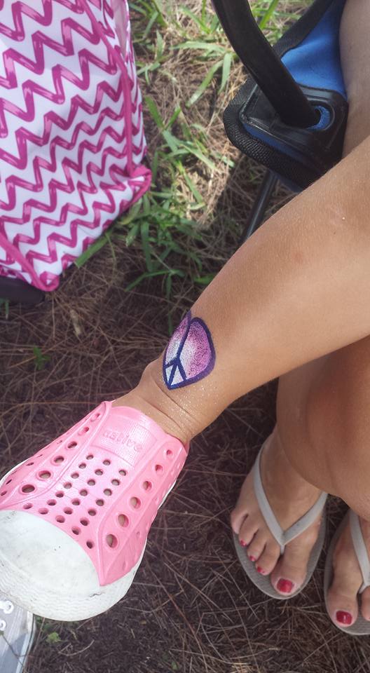 Person's arm with a peace sign tattoo, pink shoe, and flip-flops.