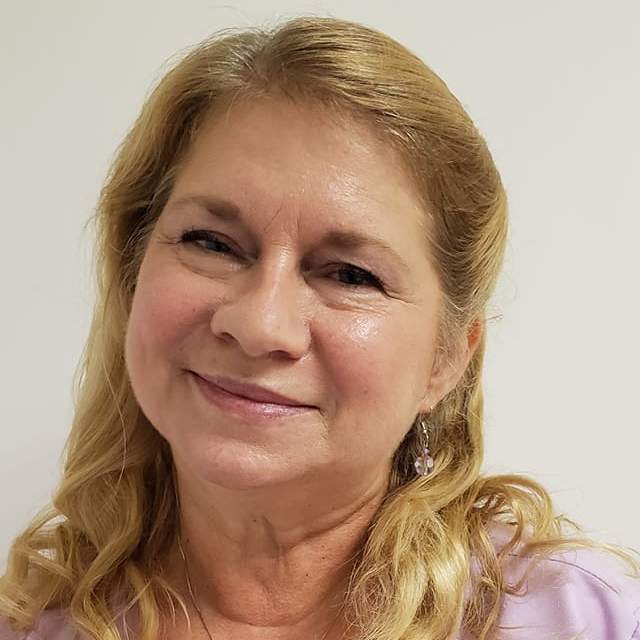 Smiling, middle-aged woman with blonde hair in a light pink top, looking to the side.