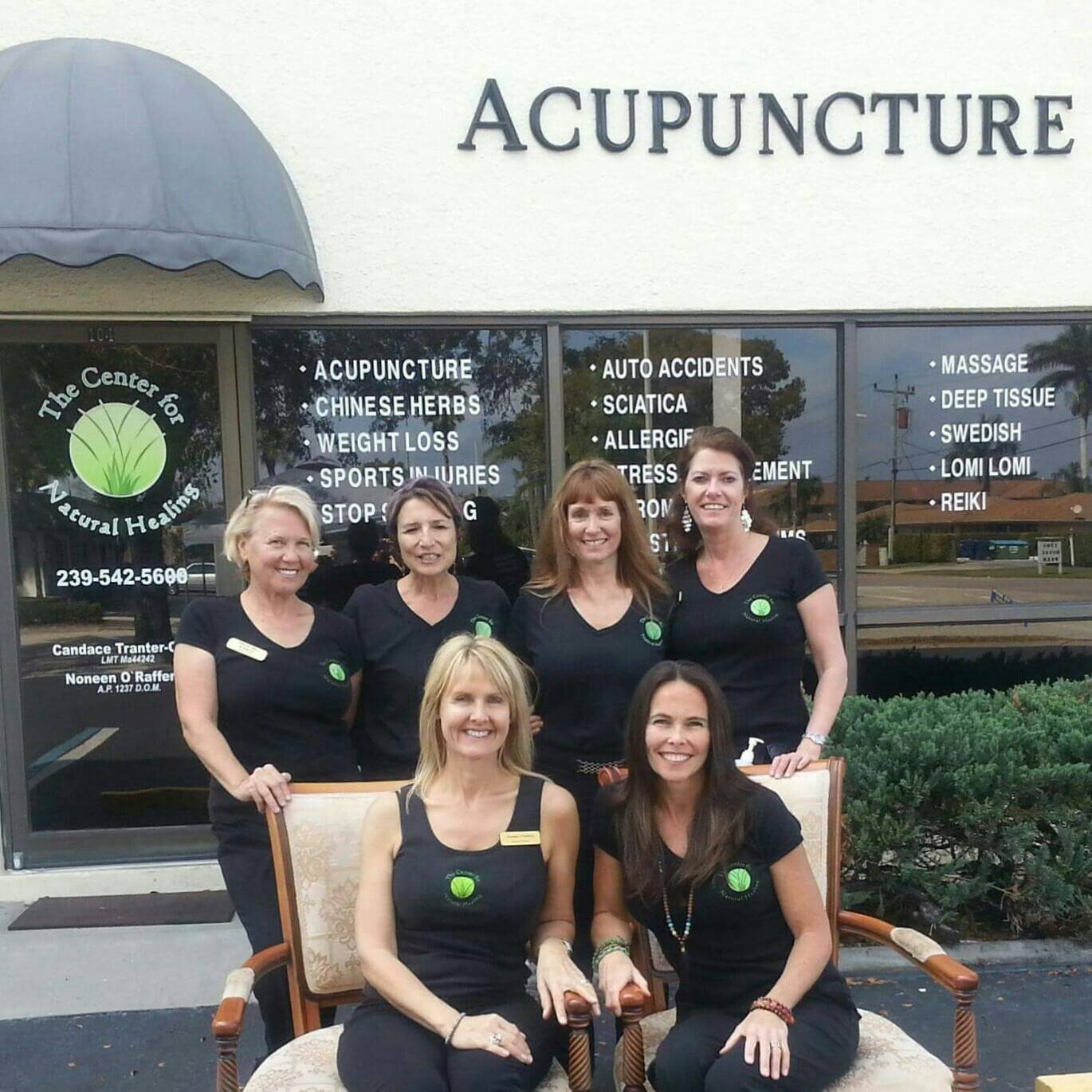 Group of women in front of acupuncture clinic. They are smiling and wearing black shirts. Clinic sign says 