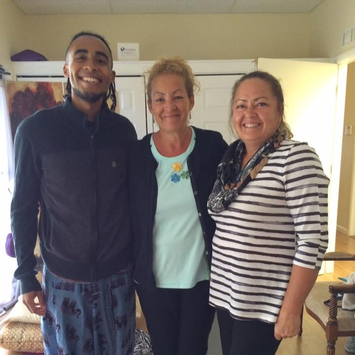 Three people smiling, posing indoors. Man in black jacket, woman in black cardigan and floral shirt, woman in striped shirt and scarf.