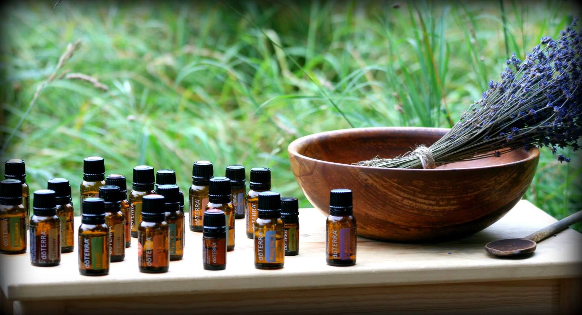 Bottles of essential oils on a wooden surface next to a bowl and lavender against a natural background.