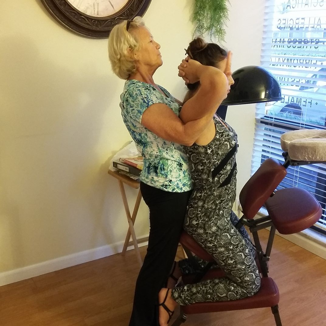 Woman giving seated massage to another woman indoors.