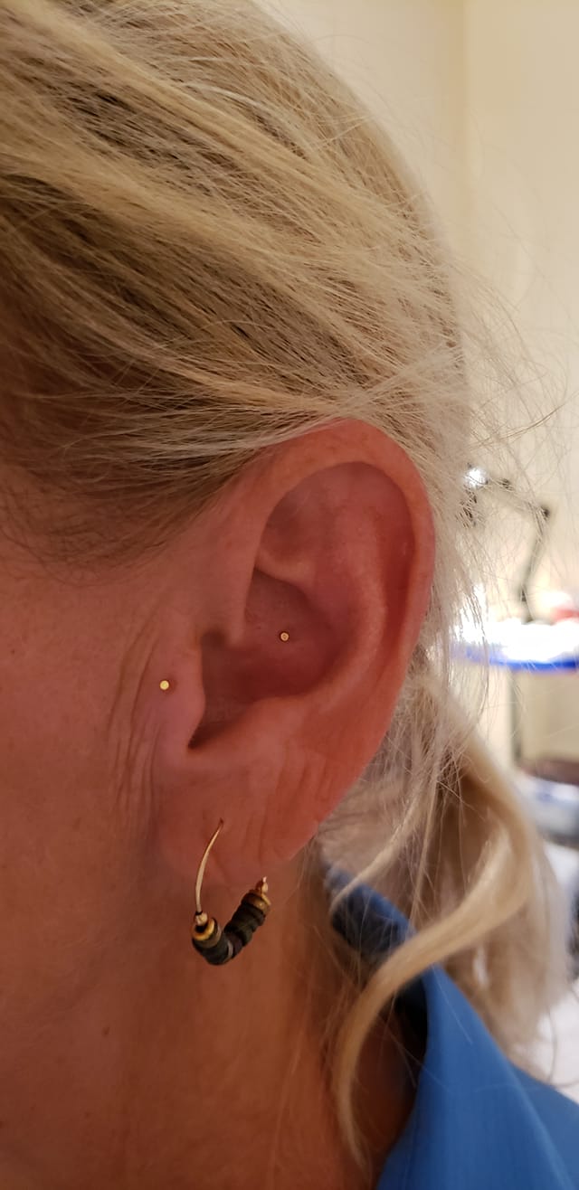 A person's ear with multiple ear piercings; wearing a small gold hoop earring with dark beads.