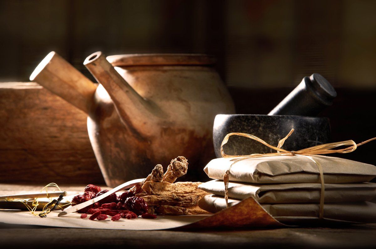 Still life of Chinese herbal medicine: teapot, mortar, wrapped herbs, and dried ingredients.