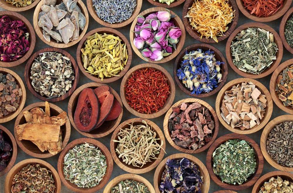 Assortment of colorful dried herbs and flowers in small wooden bowls, viewed from above.