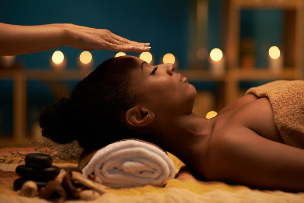 Woman receiving Reiki treatment, eyes closed, hand above her head in a candlelit room.