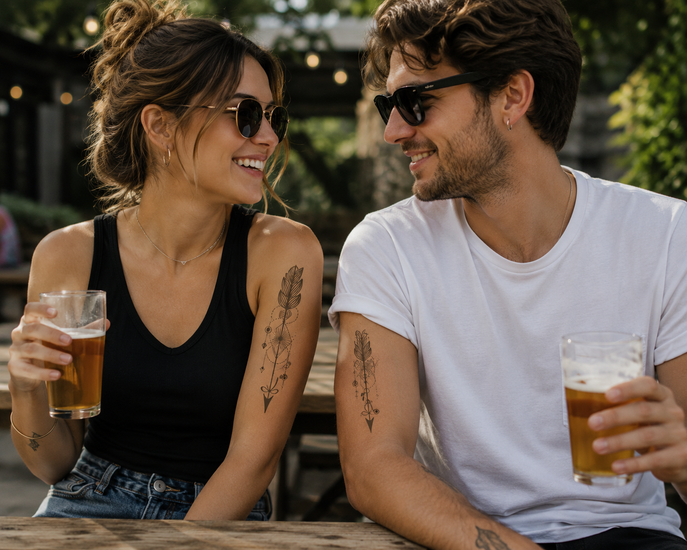 Two people in sunglasses smiling and holding drinks at an outdoor picnic table