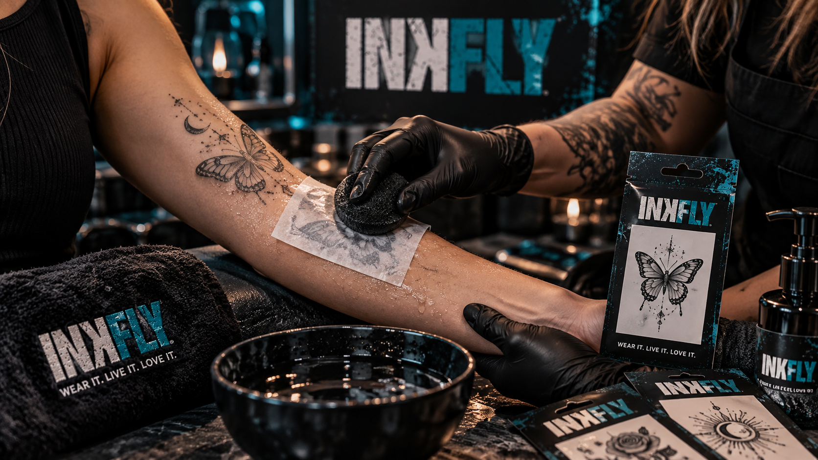 Tattoo artist in black gloves tattooing a client’s forearm at a studio table with ink bottles nearby
