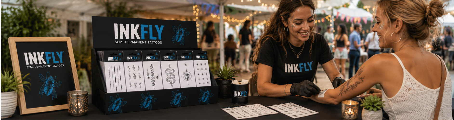 INKFLY booth at an outdoor event, with branded merchandise and two people talking at the table