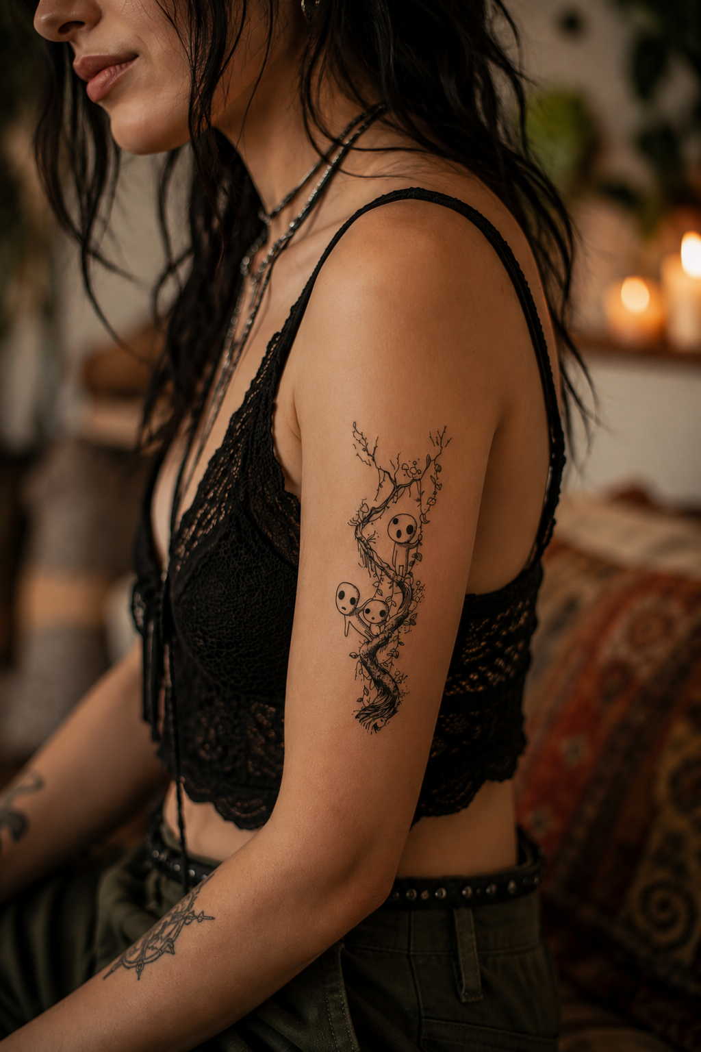 Woman in a black lace top with floral arm tattoos, seated indoors on a couch.