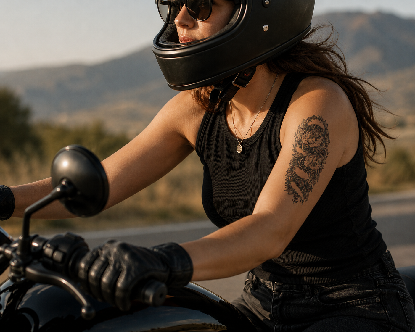Motorcyclist in black gear riding on a road, with mountains in the background.