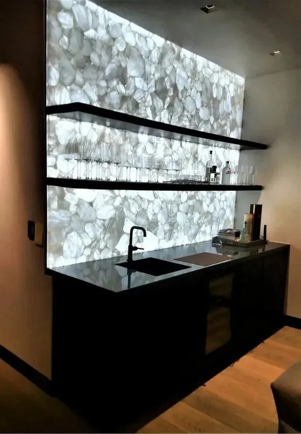 A kitchen with a sink , shelves , and a stone wall.