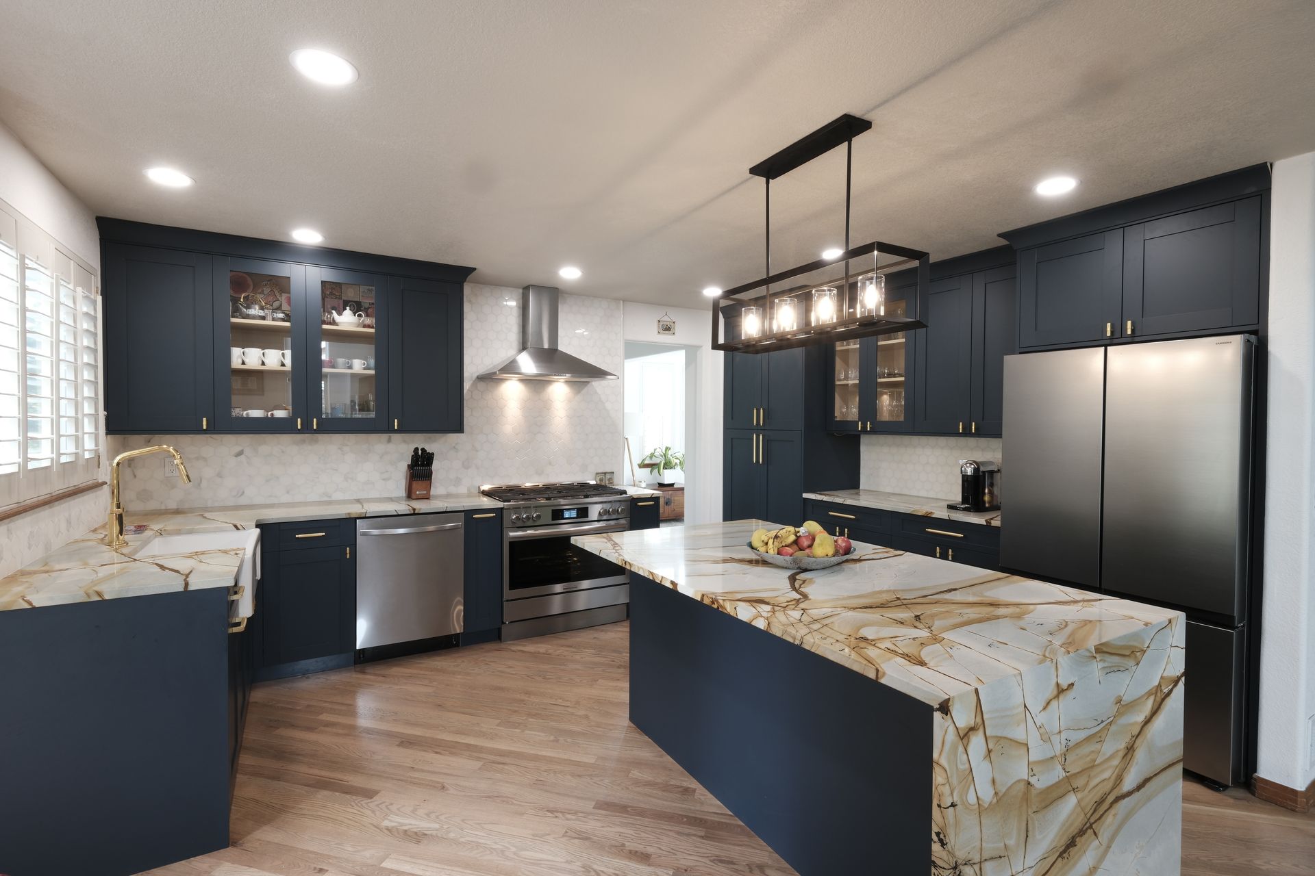 Modern kitchen with navy cabinets, marble island, stainless appliances, and wood flooring