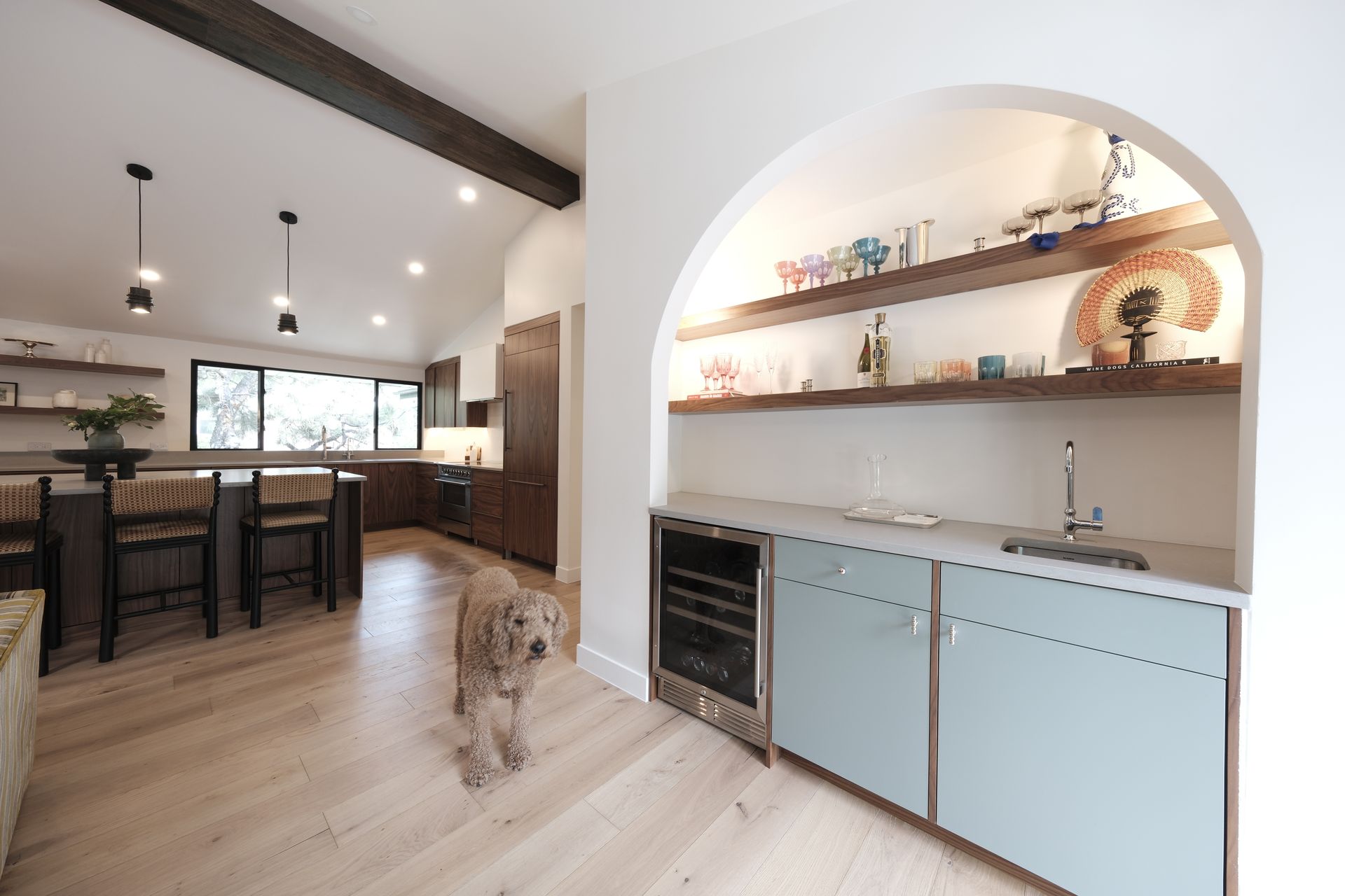 Open kitchen and dining area with light wood floors, built-in shelves, and a small dog in the center.