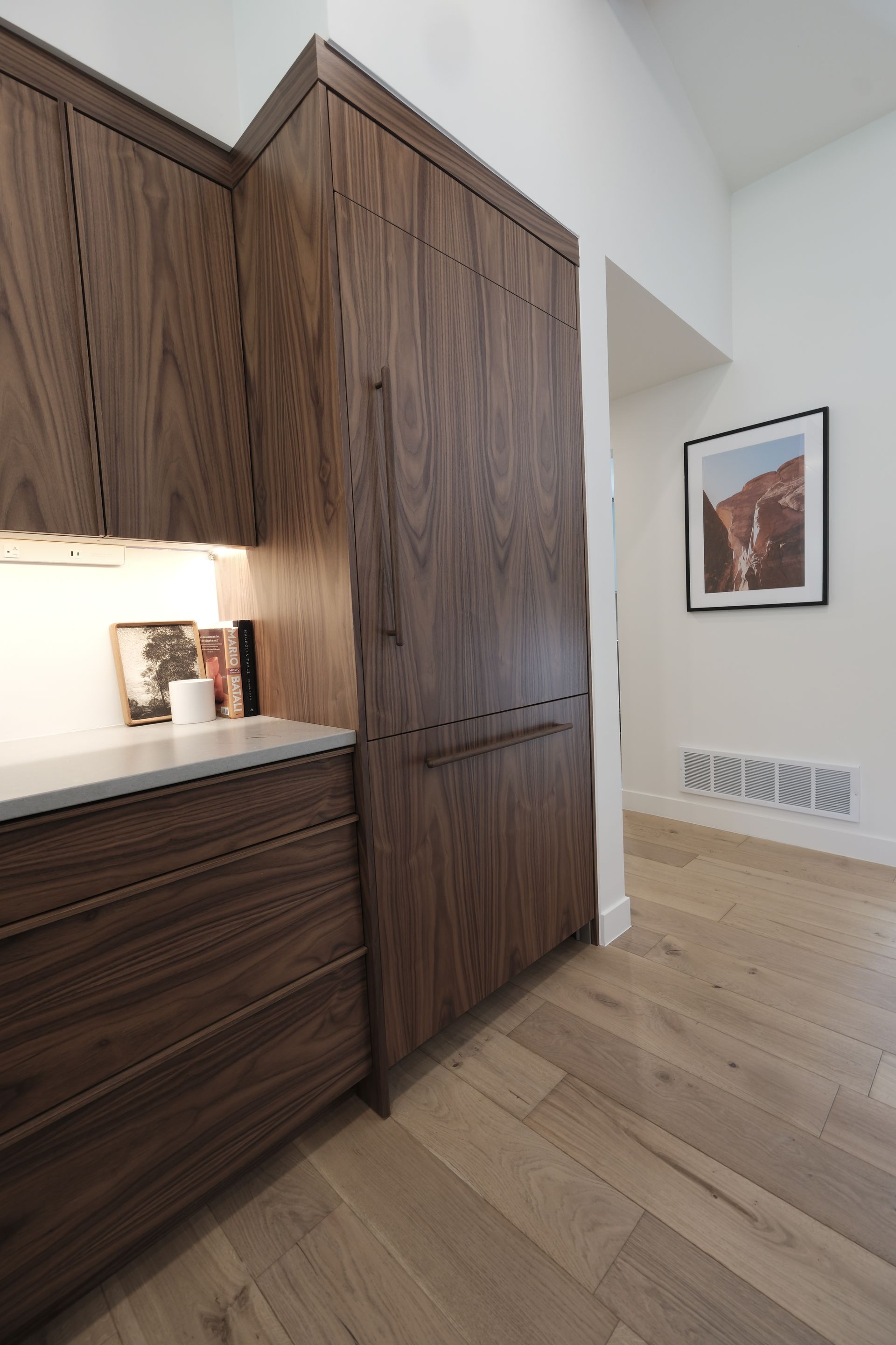 Modern kitchen with dark wood cabinets, light wood floor, and framed wall art in a bright corner.