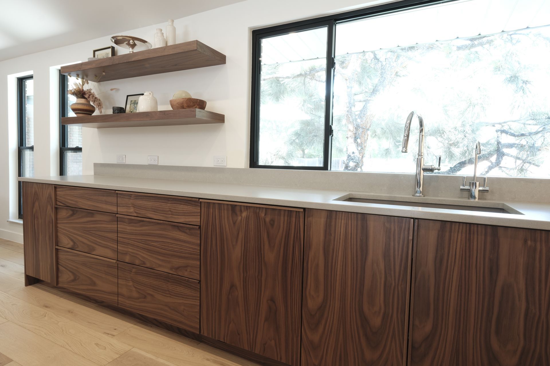 Modern kitchen with wood cabinets, white countertops, open shelves, and a large window over the sink