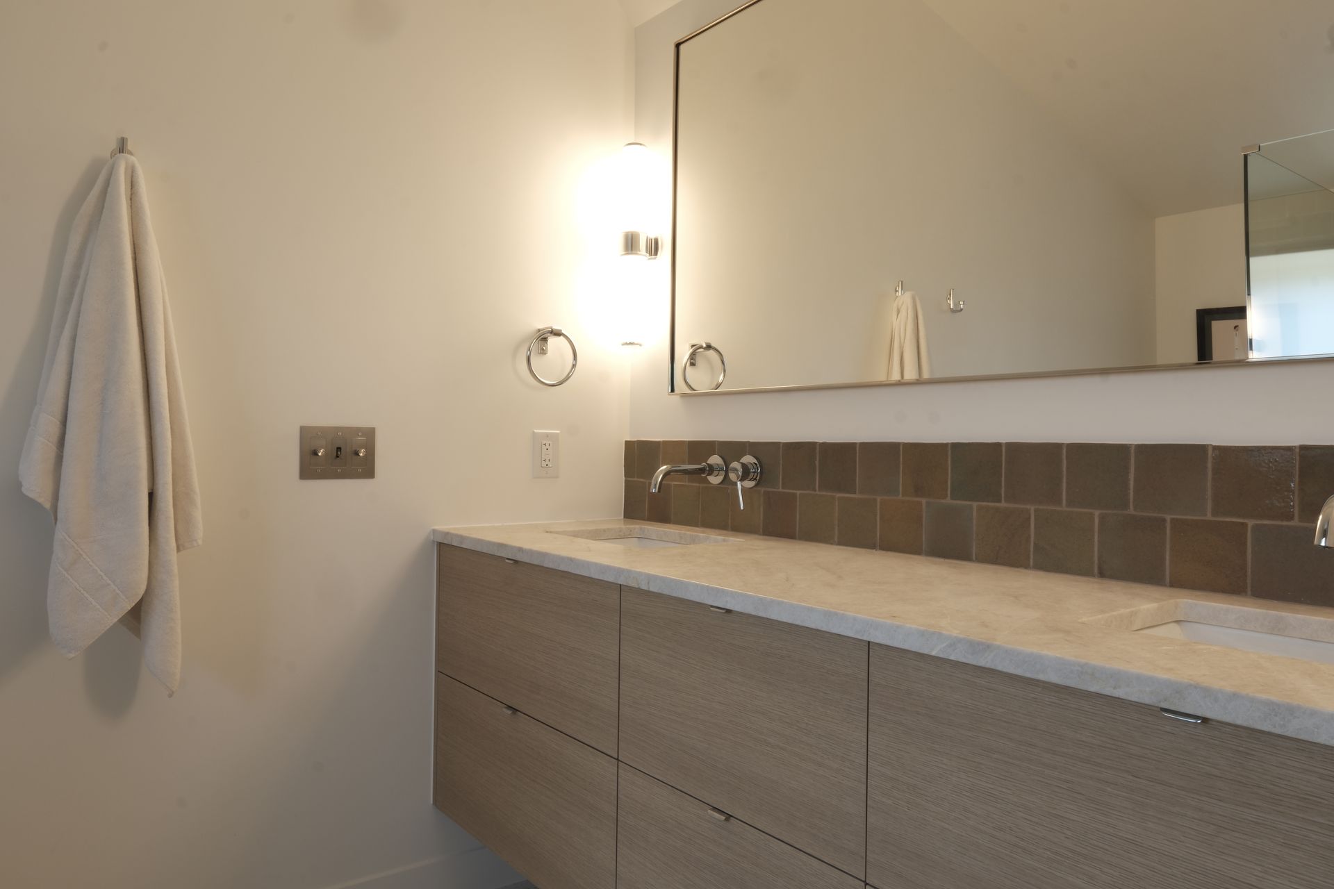 Modern bathroom vanity with mirror, tiled backsplash, towel, and wall-mounted light fixtures