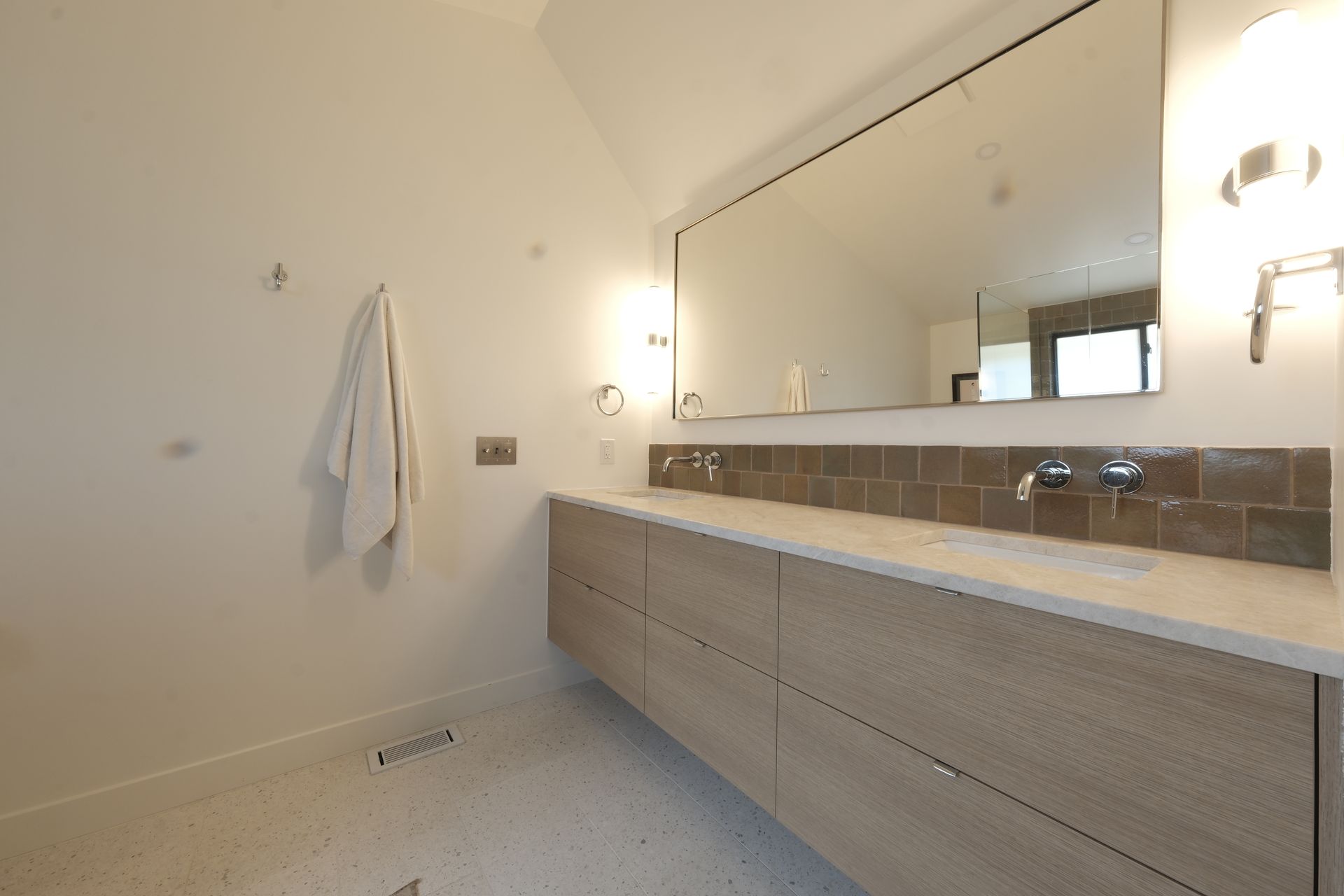 Modern bathroom with double vanity, large mirror, wall sconces, and a towel hanging on the left wall