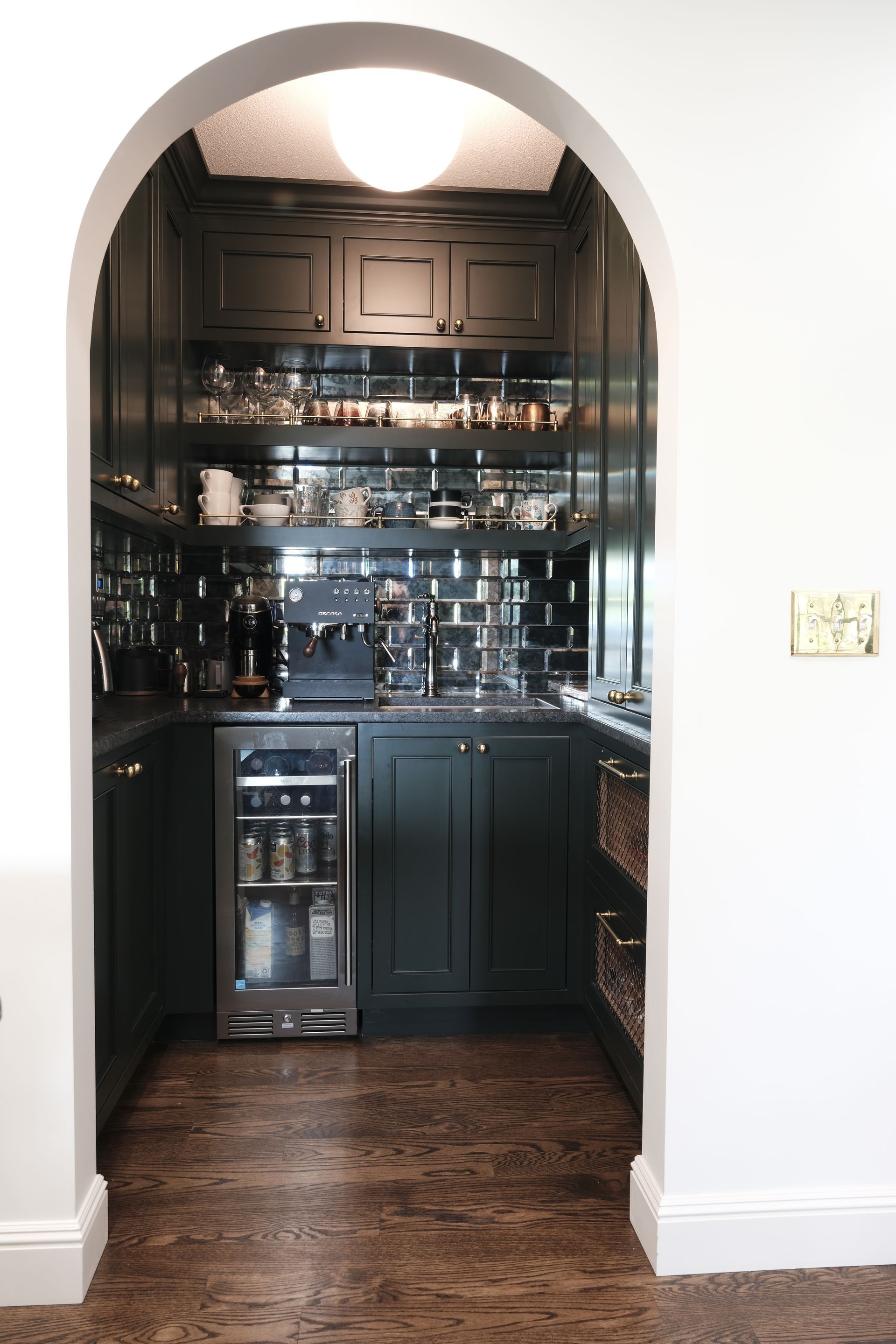 Arched doorway to a dark kitchen with black cabinets, tiled backsplash, and wood floor