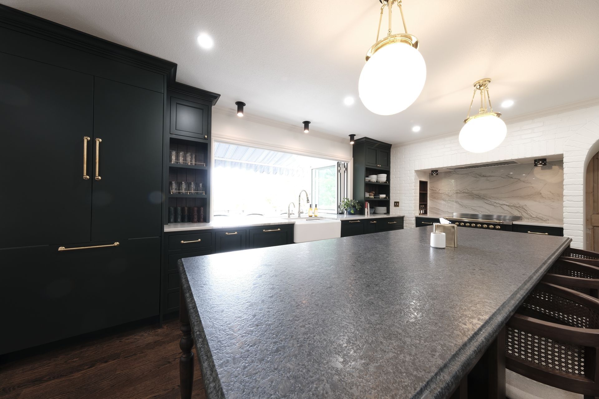Modern kitchen with a large dark island, black cabinets, white pendant lights, and a stone fireplace.