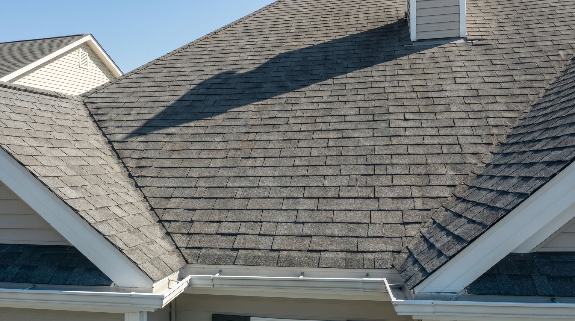 Gray shingled roof with a small white dormer against a blue sky