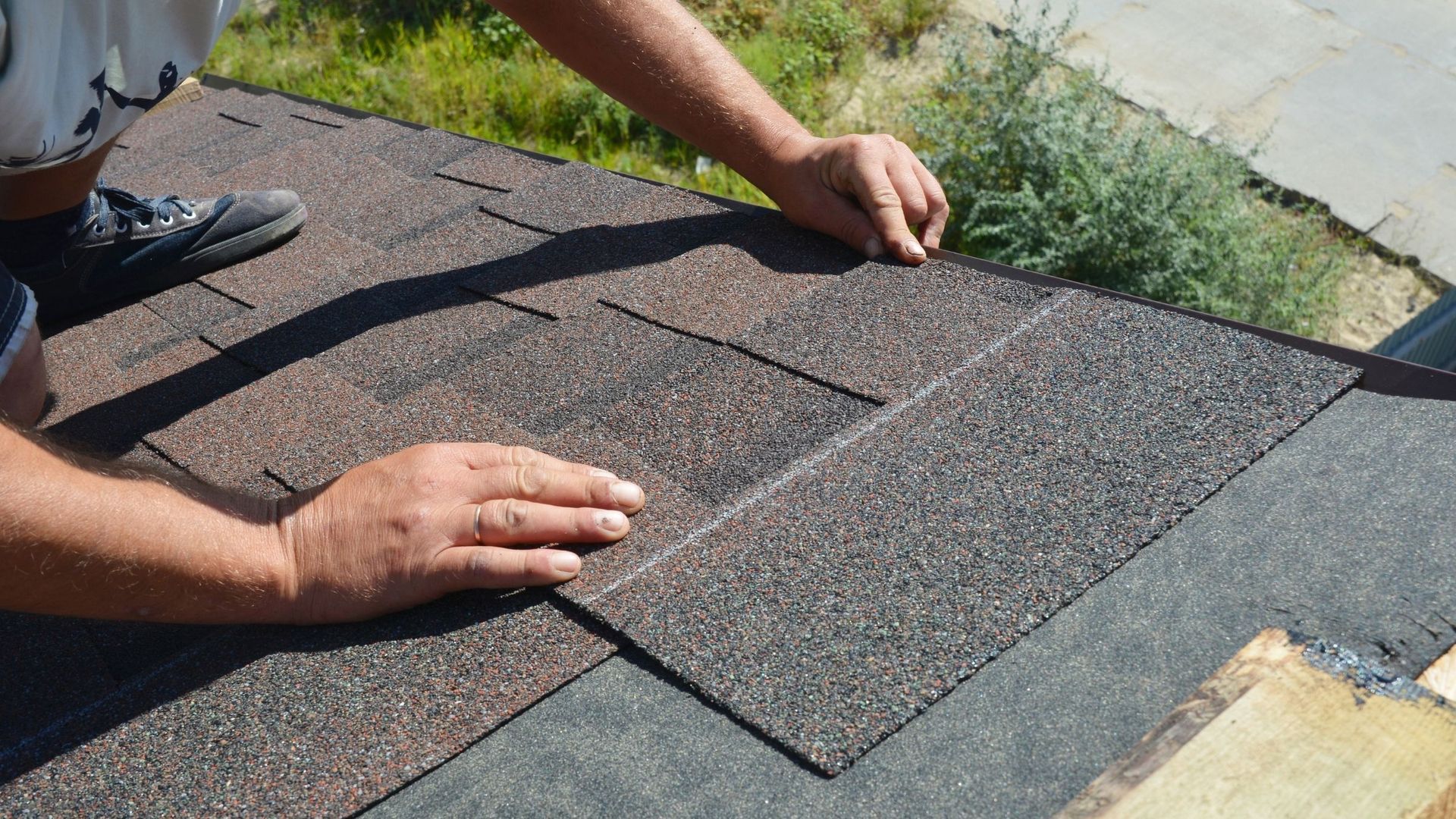 Hands installing brown asphalt shingles on a roof