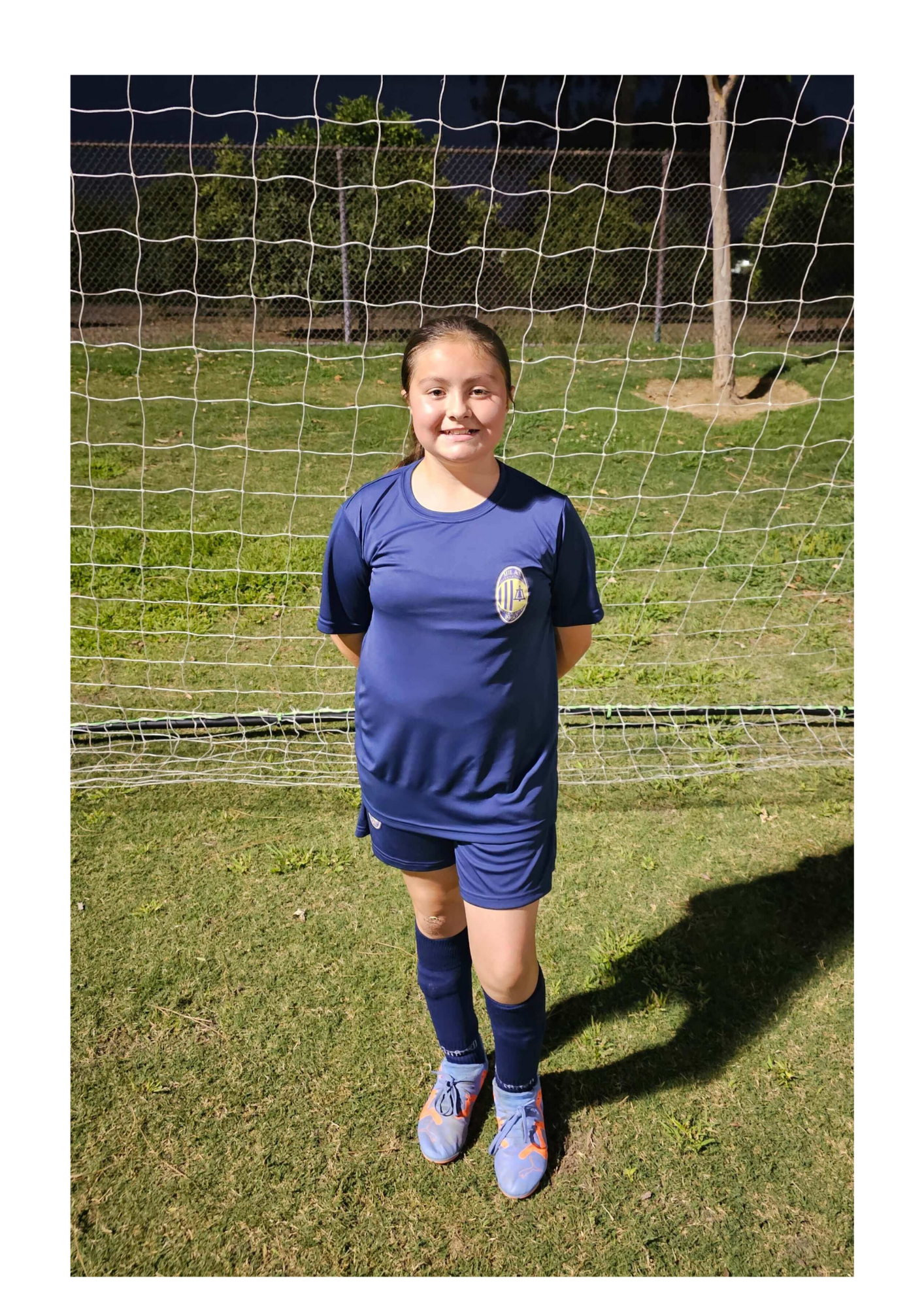 A young girl is standing in front of a soccer net on a field.