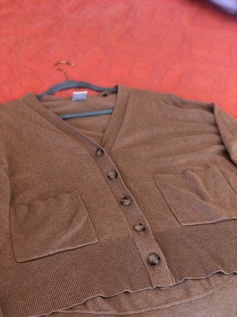 Brown cardigan sweater with buttons, hanging on a hanger against an orange backdrop.