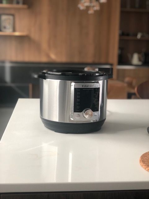 Silver Instant Pot on a white countertop in a kitchen with wood cabinets.