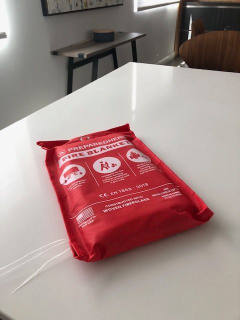 A packaged red fire blanket on a white table in a well-lit room.