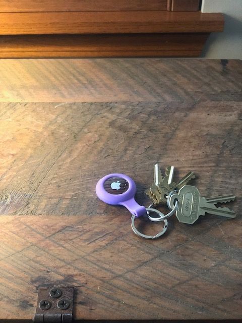 Keys with purple Apple AirTag on a wooden surface.