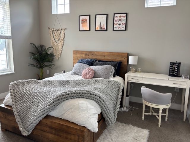 Bedroom with wooden bed, desk, art, macrame, and plants; neutral tones.
