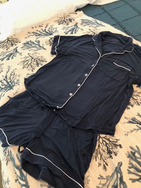 Navy blue pajama set with white piping on a bed with a coral print.