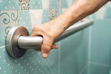 A hand gripping a silver grab bar on a light blue tiled wall for support in a bathroom.
