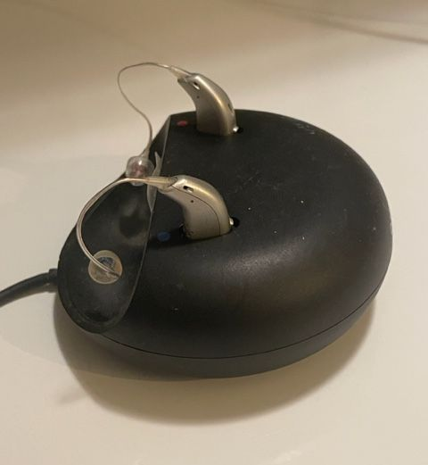 Two silver hearing aids charging on a black base.